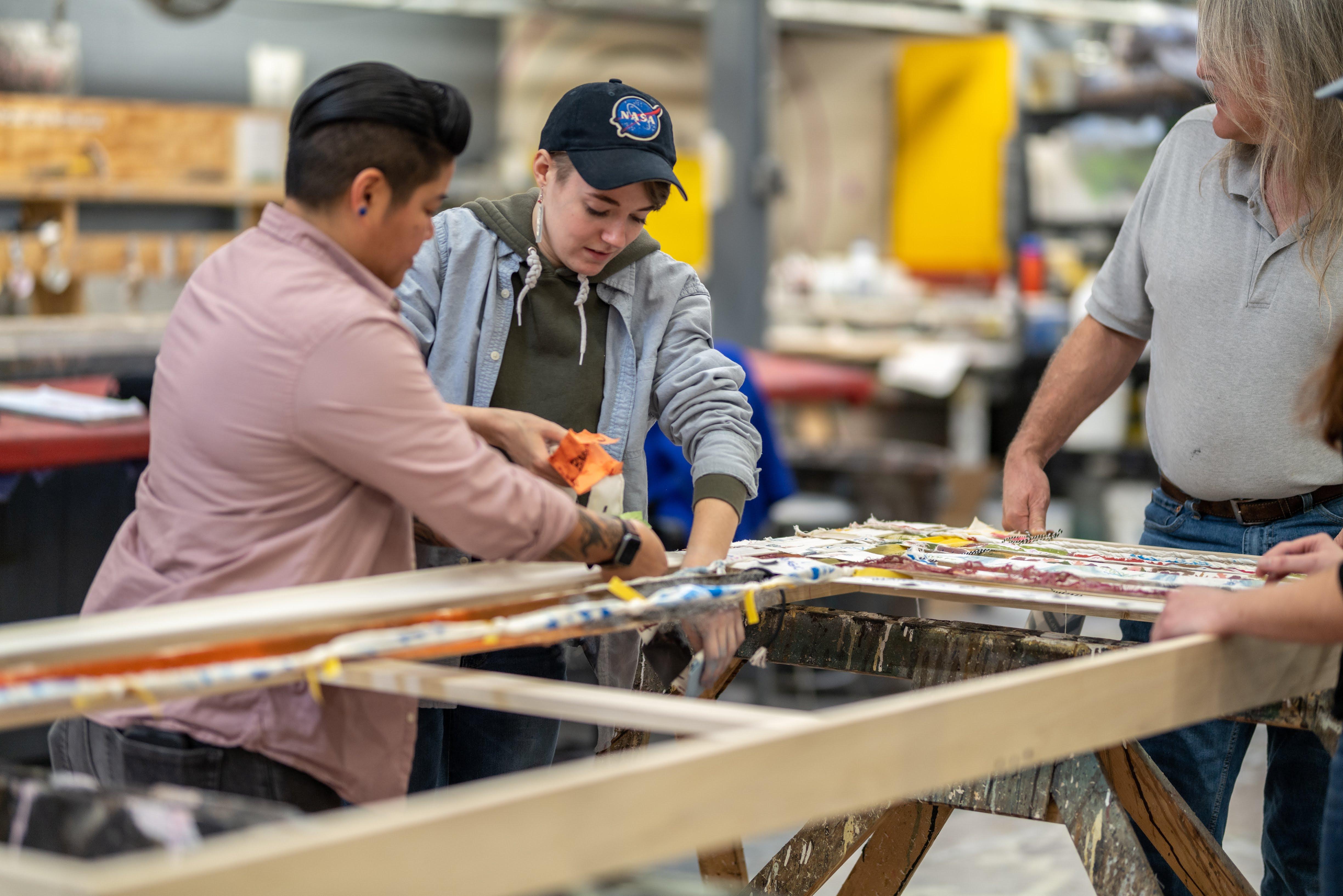 Kris Julio and Adia Matousek work on weaving strips of cloth together. / Photo: Raunak Kapoor