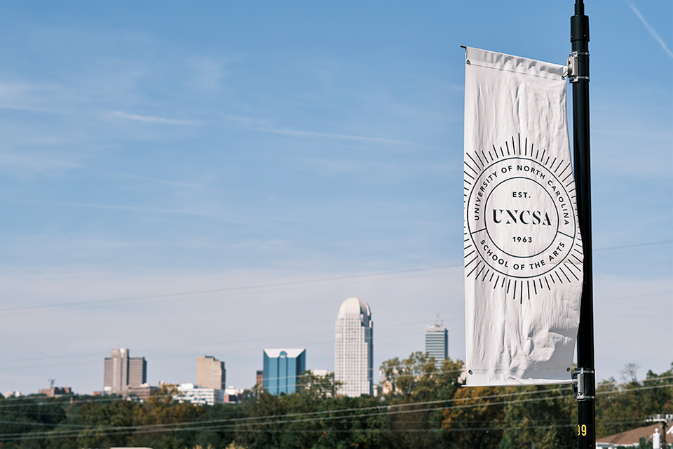 UNCSA flag with Winston-Salem skyline in the background.