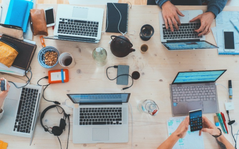 A group gathers around a table with their laptops open and phones out