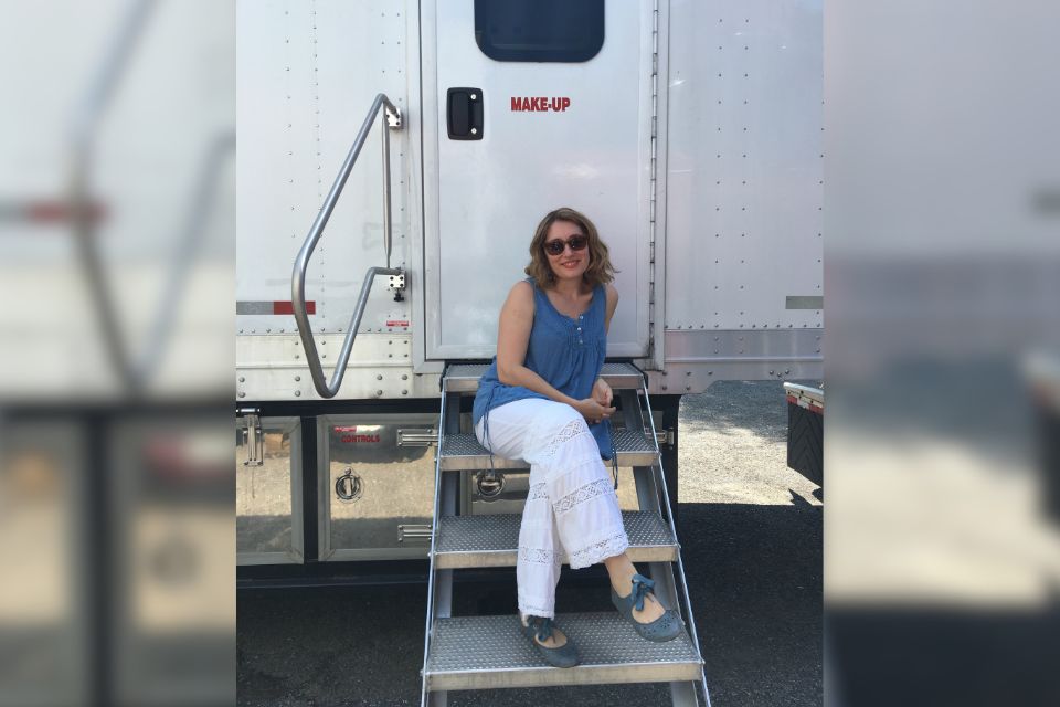 Christina Grant sitting on the steps of a makeup trailer