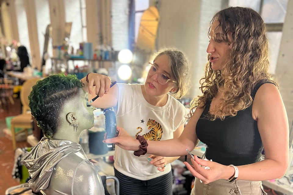 Two women applying makeup to an actor