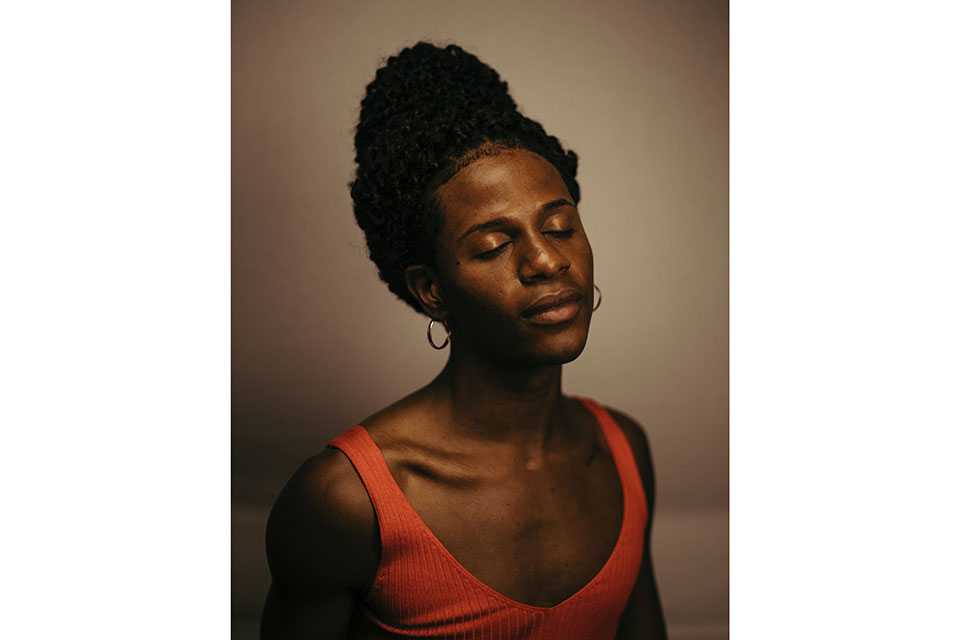 N'yomi Stewart portrait in orange shirt, eyes closed