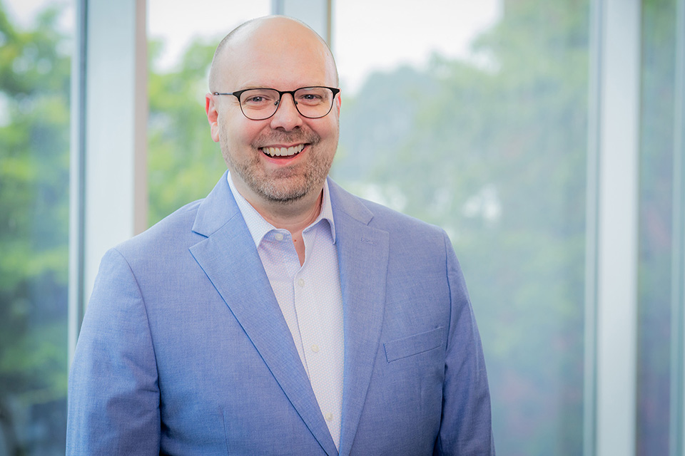Eric McEnaney smiling and posing in front of a window 