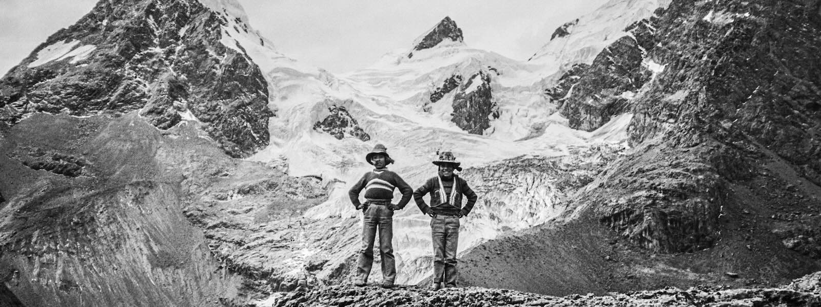 Black and white photo of two native children standing in front of a Peruvian mountain landscape.