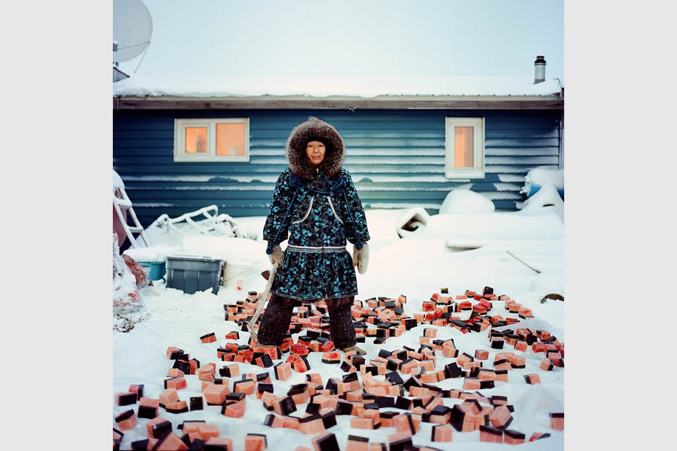 A native Alaskan woman standing outside in the snow with pieces of muktuk spread out on the ground.