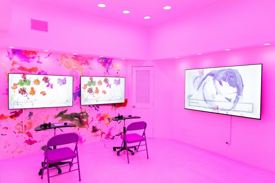 A bright pink room with two workstations with monitors projecting colorful abstract shapes.