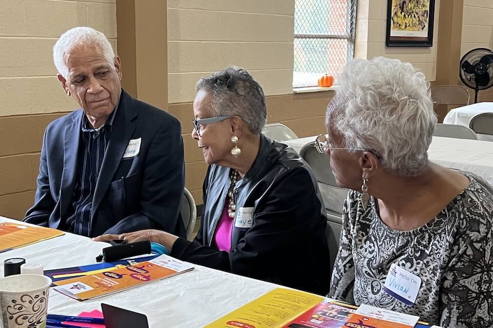 Three older people sitting at ta table and talking with each other.