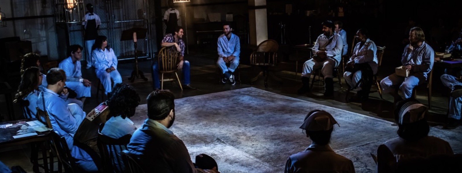 Actors dressed like patients and hospital staff sit in a circle on stage.
