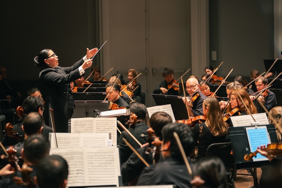 A Latina woman conducting an orchestra onstage.