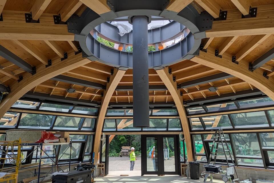 An interior photo of a building under construction. The walls are mainly glass and a ceiling shaped in a dome with an opening in the top where a chimney goes through.