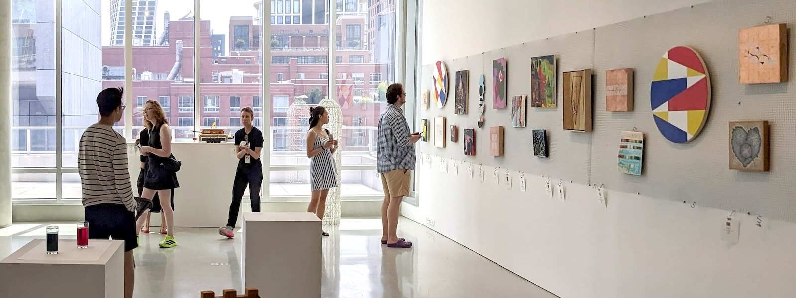 Several people in a gallery looking at a collection of artworks on a wall.