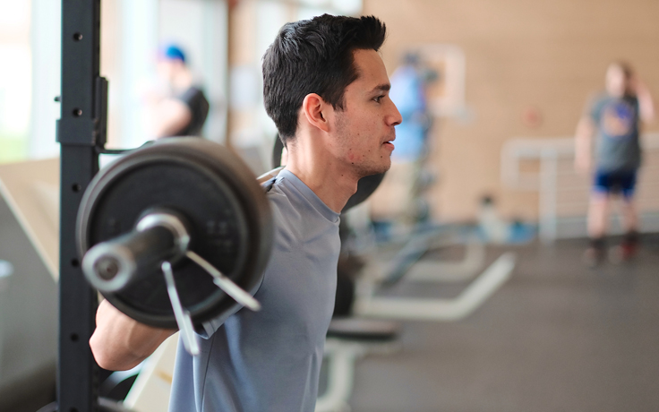 Male student lifting weights using a barbell.