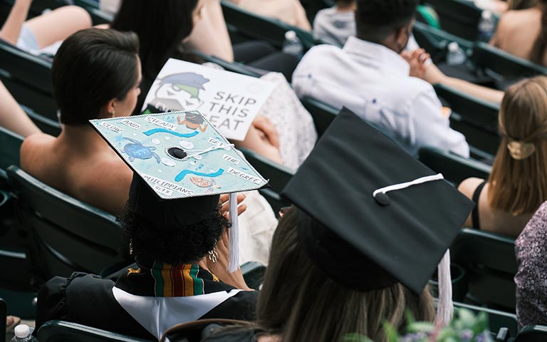 Graduating students with decorated caps sit in rows of seats