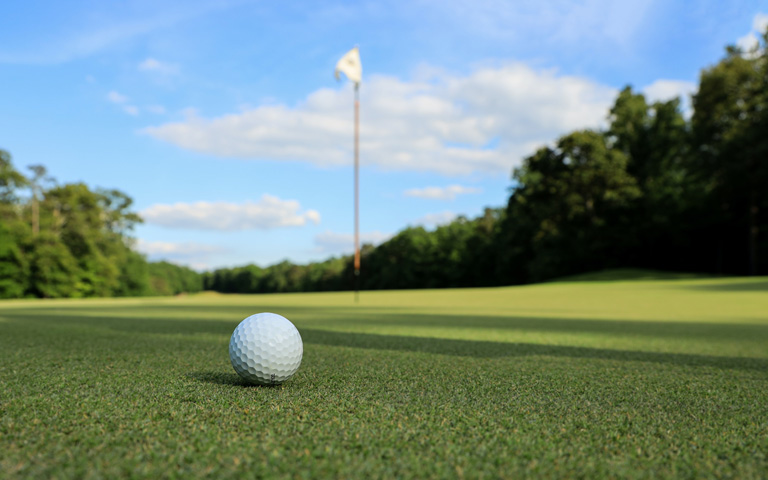 A golf ball on a green with a tee flag in the background