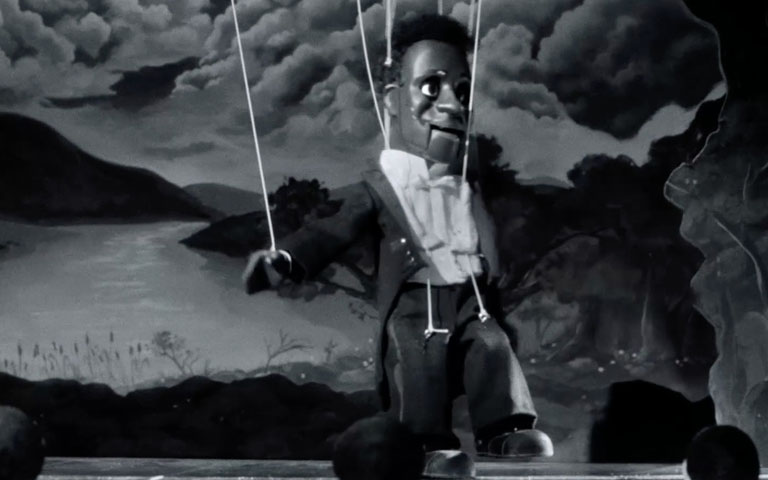 Puppet of a Black man performs on a puppet stage 