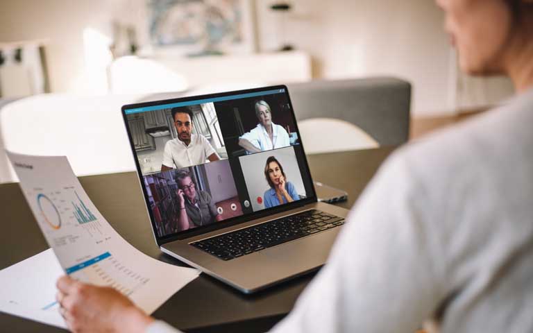 Person looking at a laptop screen with four other faces in an online meeting