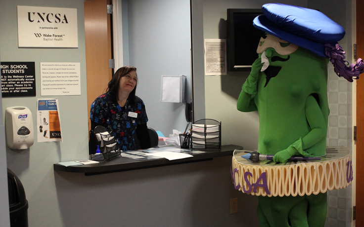 Pickle mascot at the Student Health Center holding a tissue to its face