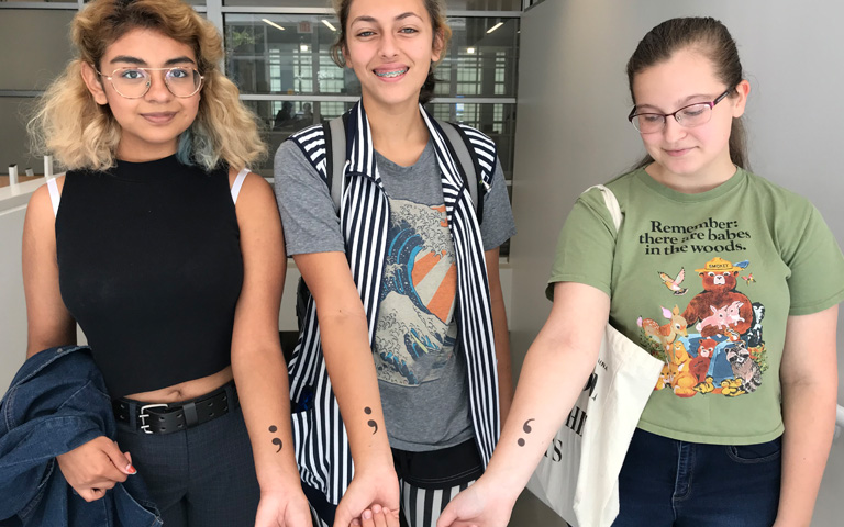 Three female student display semicolon tattoos on their arms