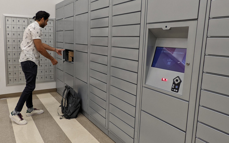 Student reaches inside a mail locker and pulls out a package.