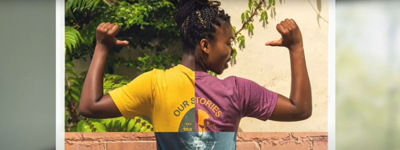 Black woman with braids shows off the back of her T-Shirt that reads ""Our Stories"