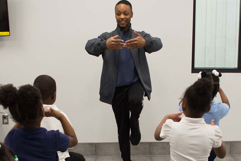 Artist Corp Member leading a group of elementary school students in a dance pose.