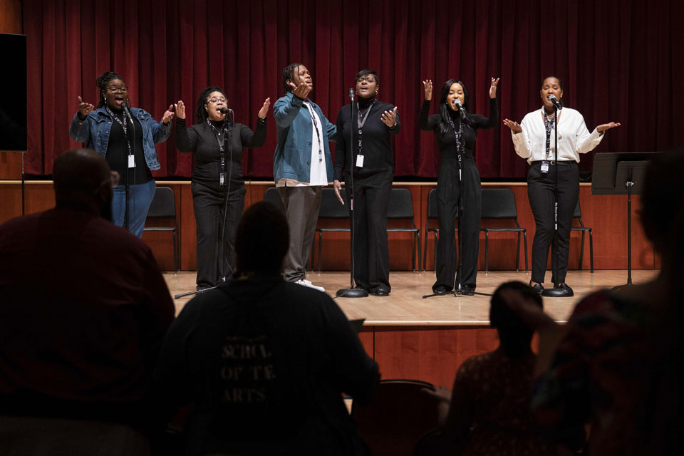 Several individuals on stage with microphones, smiling and interacting with the audience during a presentation.