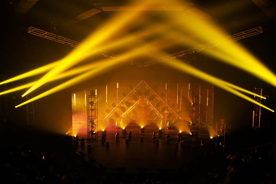 A vibrant stage illuminated by yellow lights, with a large, enthusiastic crowd enjoying the performance.