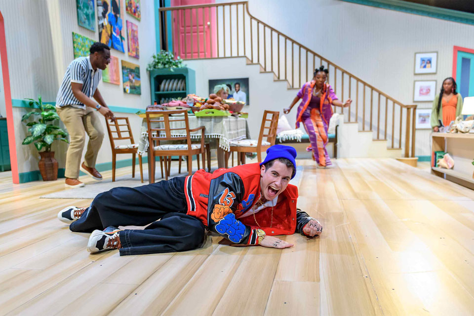 A man lies on the floor surrounded by furniture and people looking in his direction.