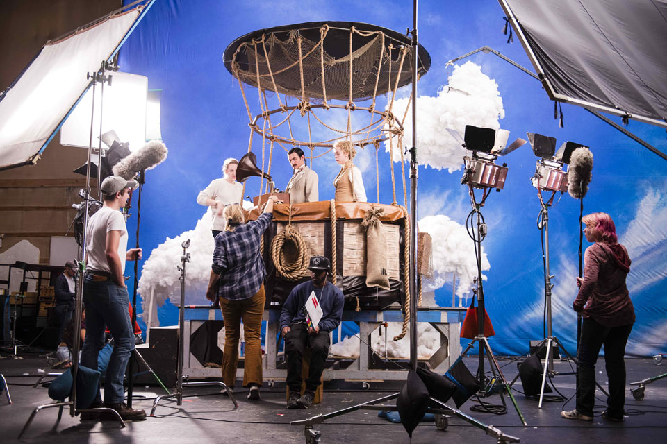 A team of individuals in a studio, smiling and interacting around a camera, showcasing a collaborative atmosphere.