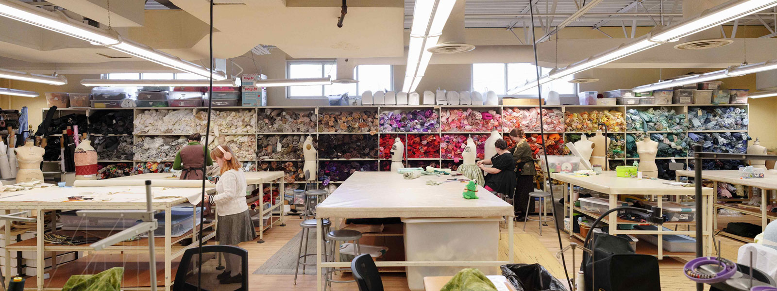 A spacious room filled with numerous sewing machines and an abundance of colorful fabric rolls stacked around.