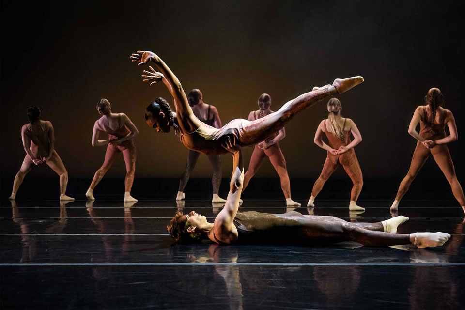 A dancer performs energetically among a group of fellow dancers, showcasing synchronized movements and vibrant expressions.