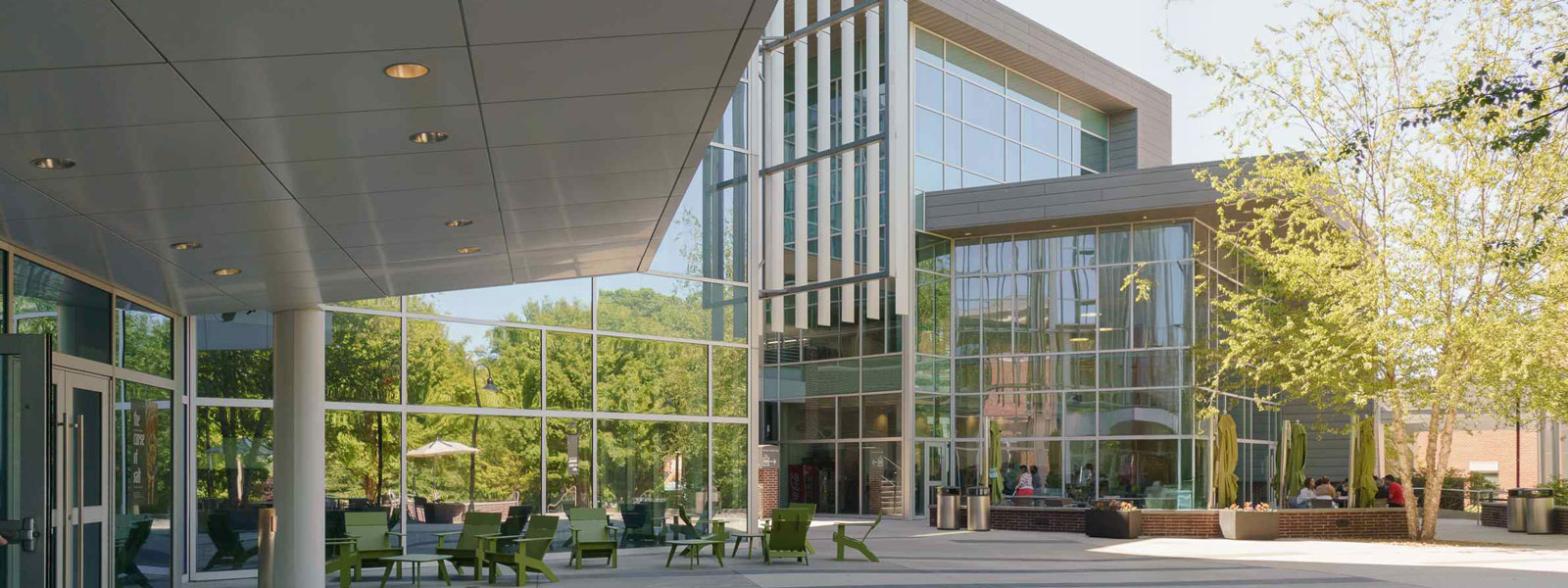 A modern building with glass walls surrounded by lush green trees under a clear blue sky.