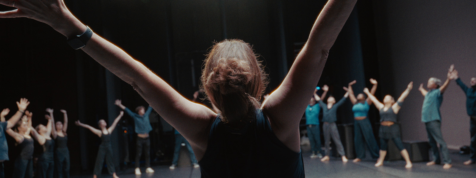 Dance instructor leads group rehearsal with raised arms