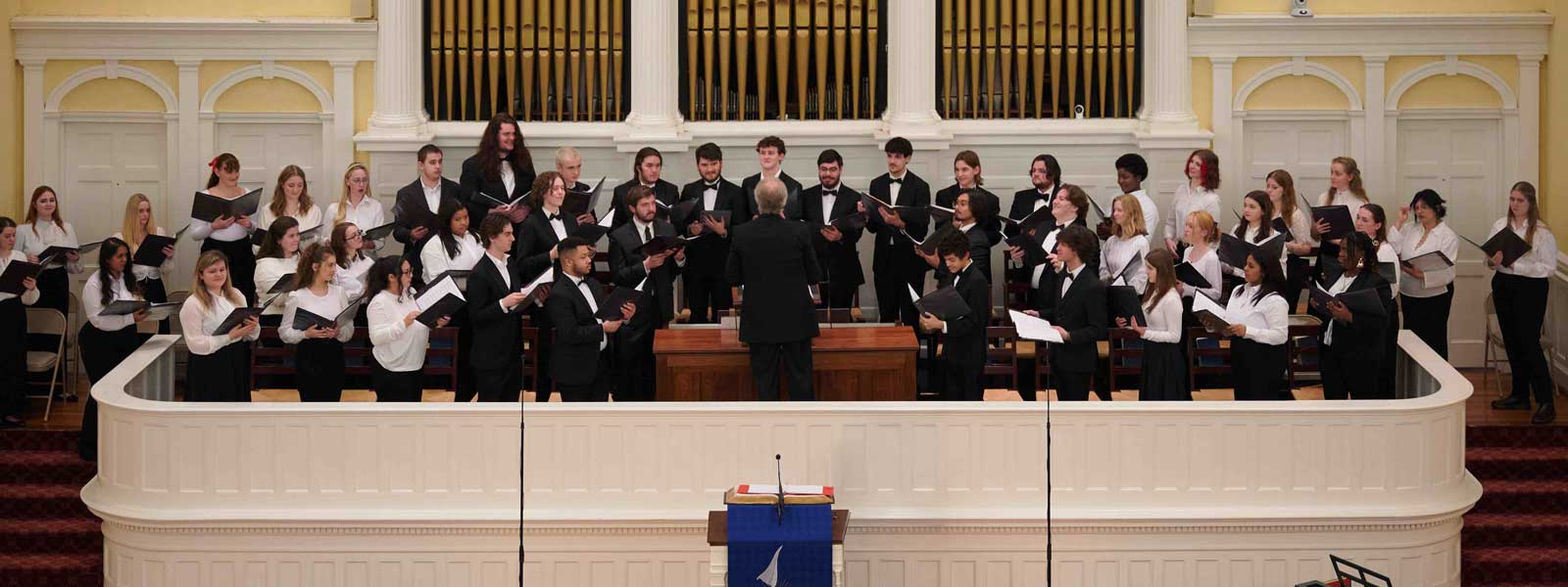 A choir stands in formation in front of a large stage, ready to perform for an audience.