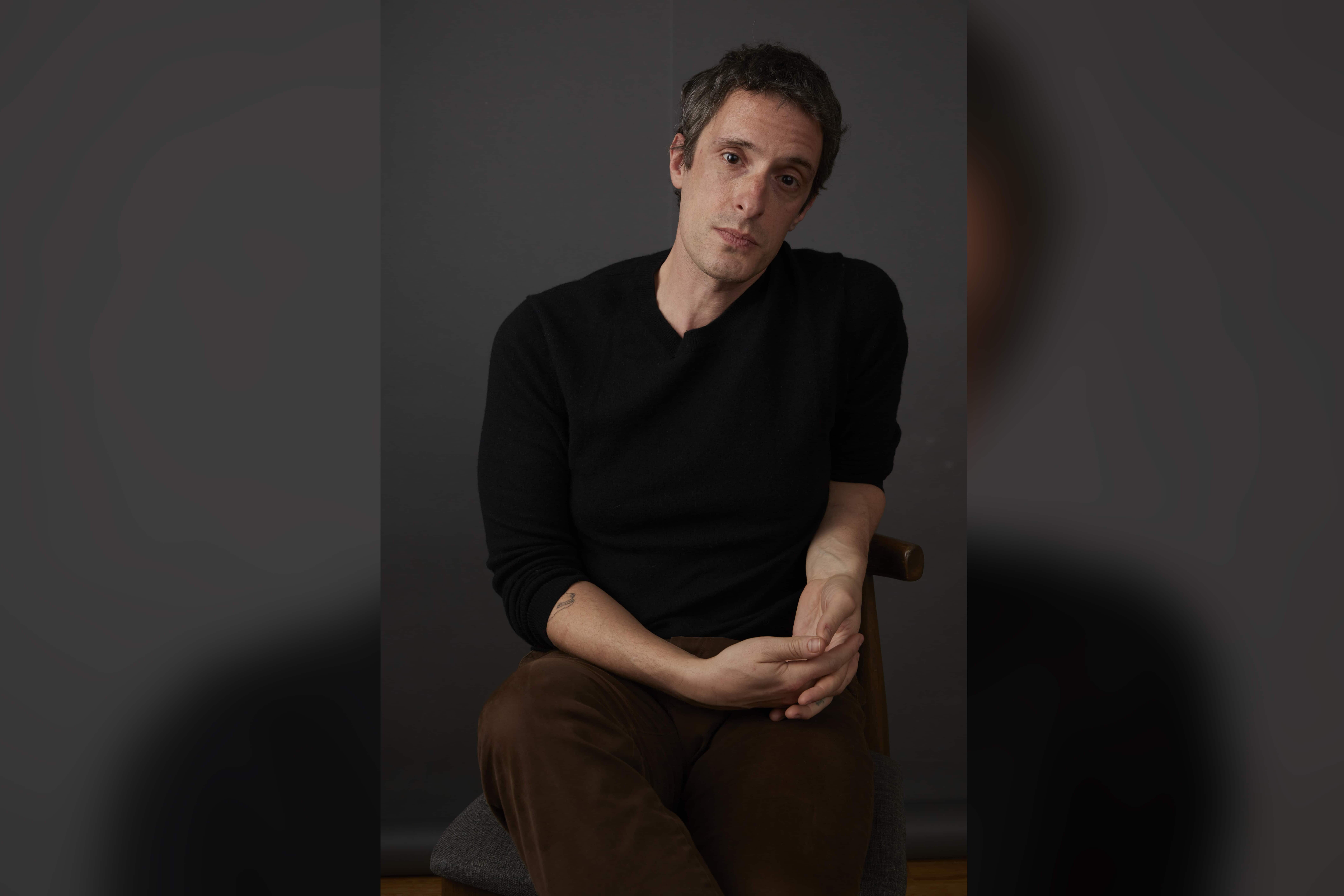 A man sits in a director's chair and looks straight ahead at the camera