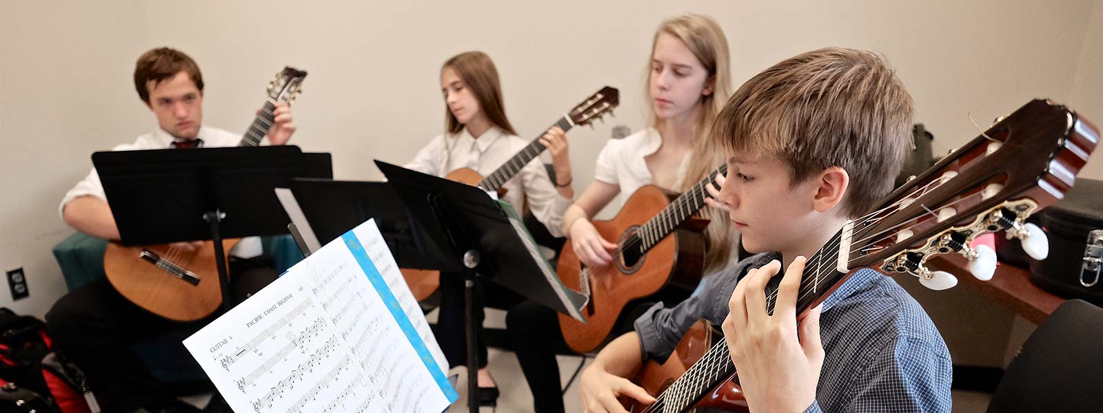 Children are seated in a circle each with a guitar in hand.