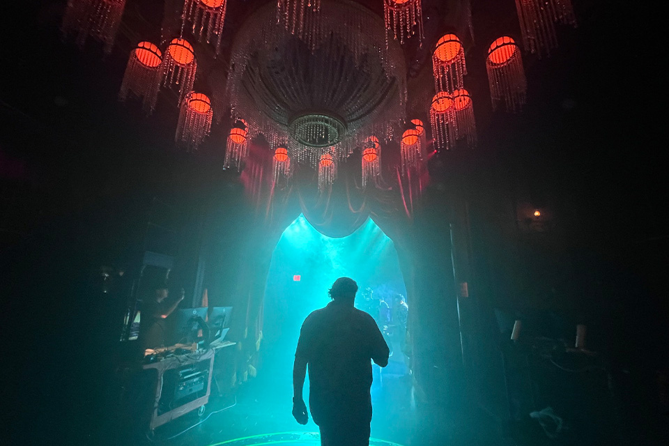 Silhouette walking backstage at NYC Masquerade under red chandeliers.