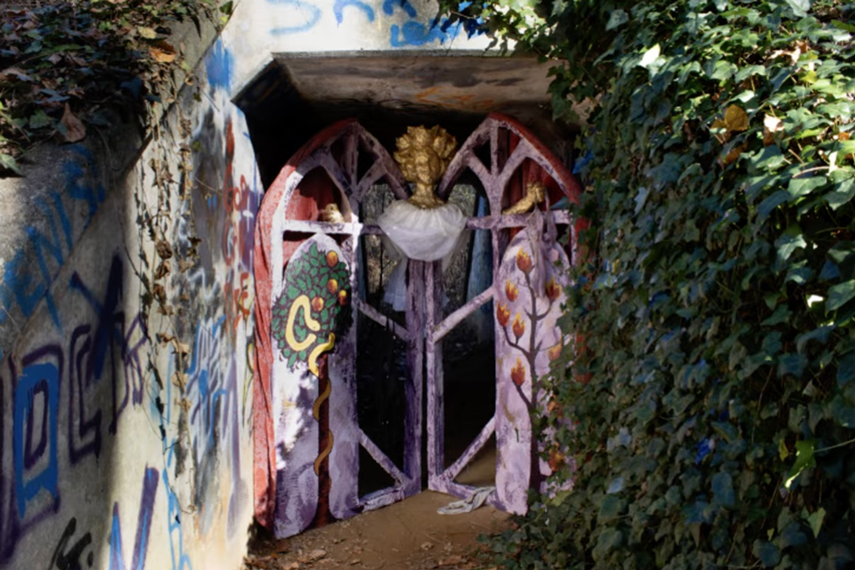 A dimly lit tunnel featuring a statue of a woman beside an ornate gate.