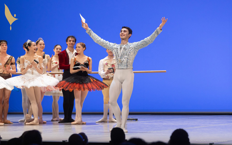 A male ballet dancer in a white outfit and tutu performs gracefully on stage during a captivating ballet performance.