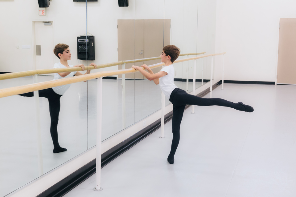  A young boy practicing ballet in a dance class, focused on his movements and surrounded by other students.  