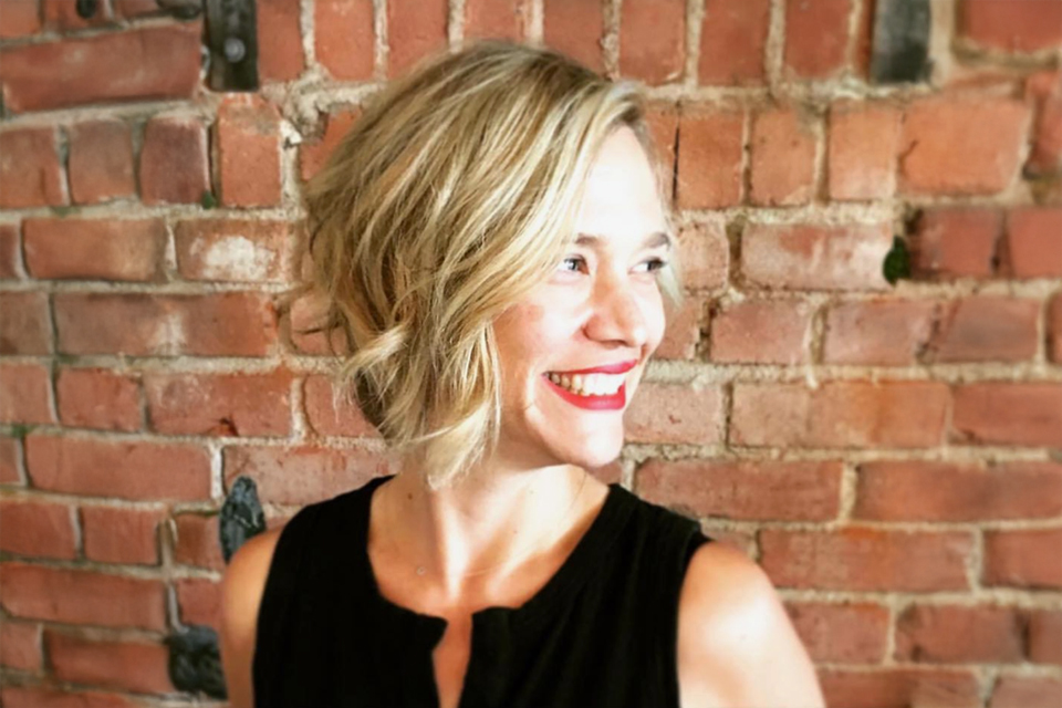 A woman smiling standing in front of the brick wall.