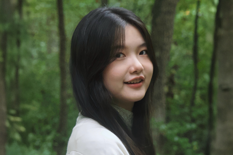 A woman looking at the camera smiling with greenery in the background.