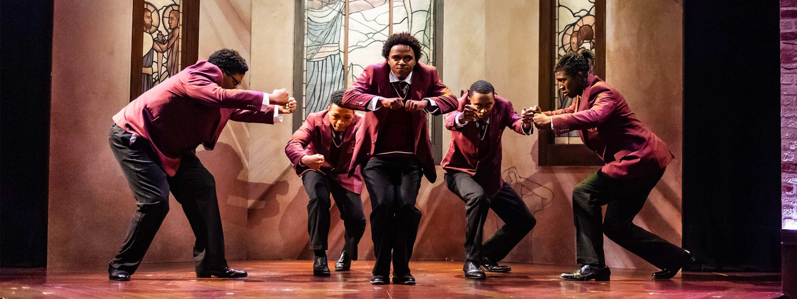 A group of men in red suits performing a lively dance on stage, showcasing synchronized movements and energetic expressions.