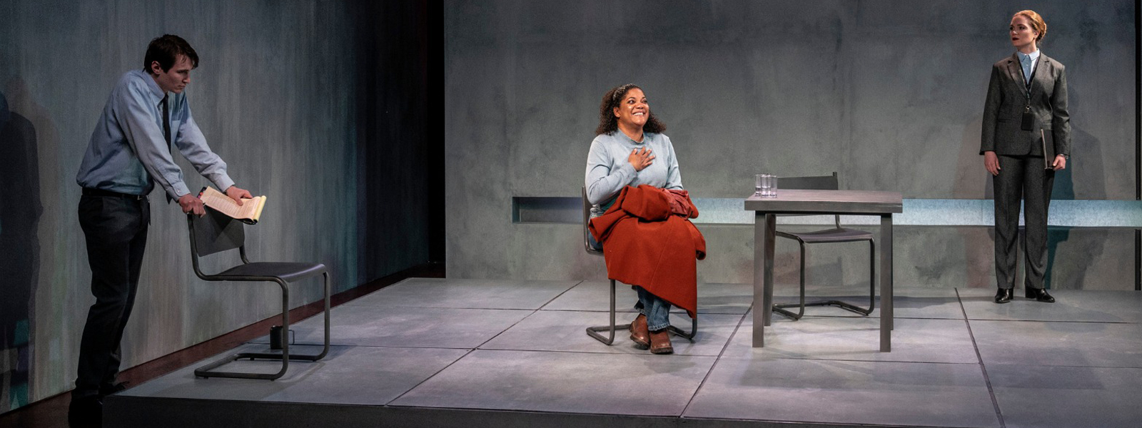 A scene from the play featuring three people seated on chairs in a room, engaged in conversation.