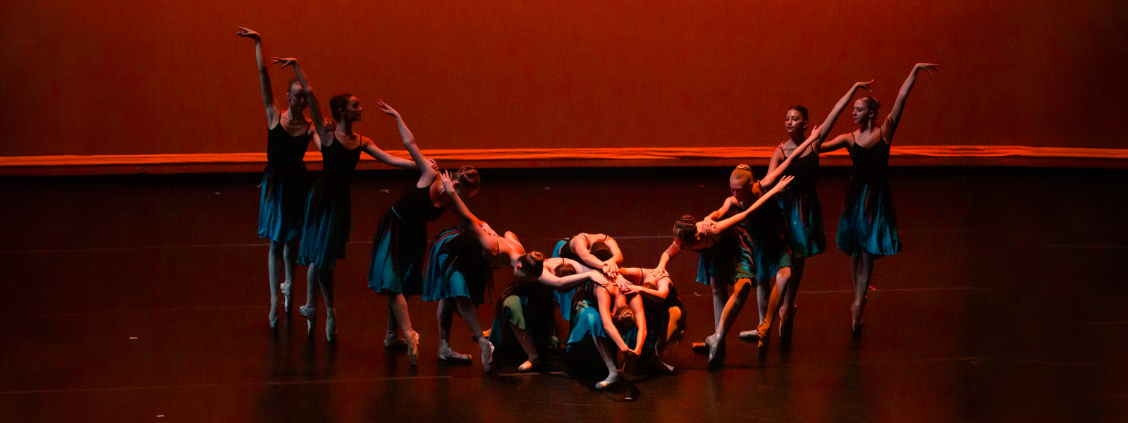 A group of dancers in colorful costumes performing energetically on stage under bright lights.