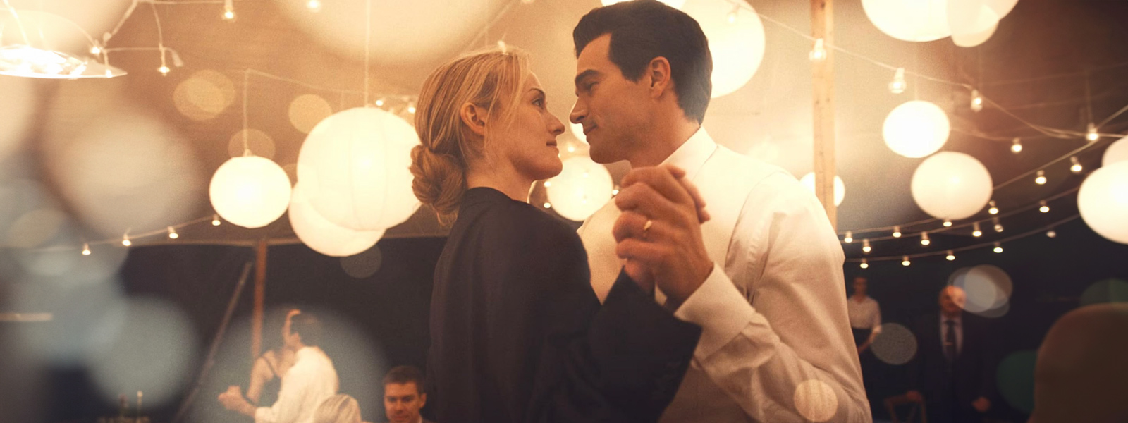 A man and woman dance joyfully in front of a backdrop of glowing string lights.